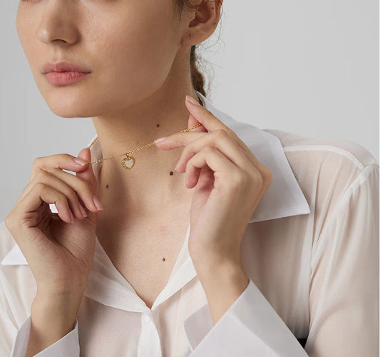 Woman wearing a delicate necklace with a heart pendant against a plain background