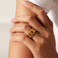 Hand wearing a gold chain ring on a neutral background